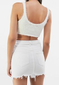 En person ses bakifrån, klädd i en fluffig vit cropped topp och en kort vit slitna denimkjol, vilket visar en avslappnad outfit.