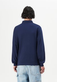 Camisa polo de manga larga en color navy con un corte relajado, que cuenta con un collar clásico y puños acanalados, combinada con unos jeans holgados de color azul claro.