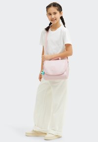 Borsa a tracolla rosa chiaro con patta, materiale in tessuto e accessori in metallo argentato. Include un ciondolo colorato attaccato alla cerniera.
