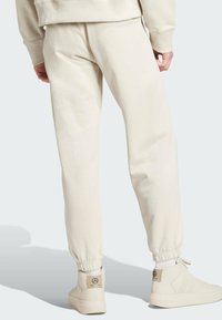 Beige sweatpants with a tapered fit and elastic cuffs, paired with cream high-top sneakers featuring perforated accents and branded logo.