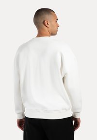 Sudadera blanca hecha de material suave, con un diseño sencillo, cuello redondo, puños y dobladillo de canalé, y un ajuste relajado.