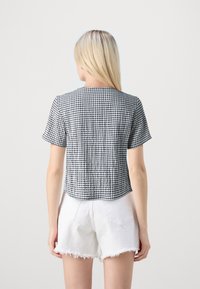 Blusa de manga corta a rayas en blanco y negro con escote redondo, diseño cropped, fabricada en tejido liviano, combinada con shorts blancos.