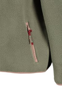 Close-up van groen fleece-stof met een roze rits en een rood trekkoordje op een zak van een jas.