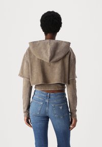 Zkrácená mikina s kapucí v světle hnědé látce se vybledlým vzorem; nošena přes tričko s dlouhým rukávem a spárována s modrými džíny.