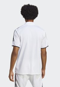 Polo shirt sportivo bianco con accenti neri, maniche corte e colletto, realizzato in un materiale liscio e leggero. Presenta strisce laterali a contrasto.