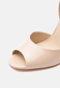 Μπεζ παπούτσι με λουστρίνι, ανοιχτή μύτη και ψηλό τακούνι, με λεία επιφάνεια και ανοιχτό καφέ σόλα.