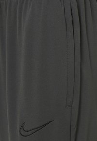 Mørkegrå atletikshorts lavet af glat stof, med elastisk taljebånd og en sort Nike-logo broderet på siden.