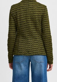 Grüner, gemusterter Blazer mit strukturiertem Webmuster, langen Ärmeln und tailliertem Schnitt. Kombiniert mit hellblauen, weit geschnittenen Jeans.