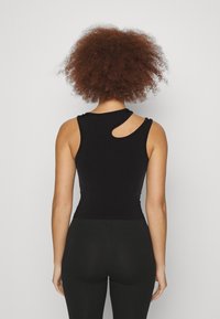 Top senza maniche nero con un taglio curvo sulla spalla, realizzato in un tessuto liscio e elasticizzato, abbinato a leggings neri.