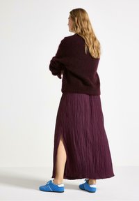 Bordeauxfarvet, struktureret, lang nederdel med en sideslids, parret med en løs, mørk sweater og blå sko med hvide detaljer.