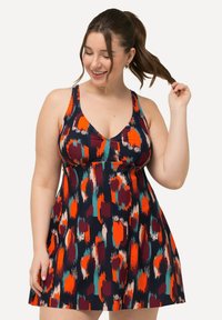 La robe présente un décolleté en V profond, un design sans manches et un imprimé abstrait multicolore sur un fond sombre. Tissu doux et léger.