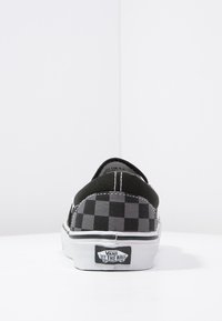 Chaussure slip-on en toile  à damier noir et gris avec une semelle en caoutchouc blanche et des coutures contrastées ; présente le logo Vans sur le talon.