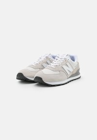 Zapatillas de deporte gris claro con parte superior de ante y malla, que presentan un acento en blanco y gris, suela de goma negra y sistema de cordones tradicional.