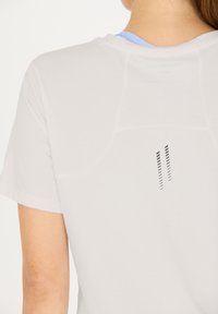 Vit sportskjorta med kort ärm, med en blå innerkrage och svarta randiga detaljer på baksidan. Slätt, lättviktigt tyg.