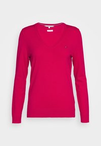 Maglione a V in cotone rosa brillante, con maniche lunghe e un piccolo logo sul petto. Texture liscia e design aderente.