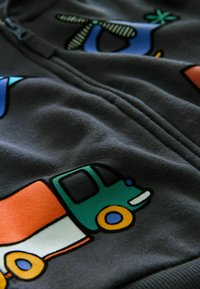 Grå zip-up sweatshirt med farverige lastbiler og abstrakte designs. Fremstillet af blødt stof med glat tekstur og distinkte grafiske mønstre.