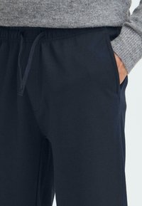 Temno modri trenirki iz teksturiranega materiala z elastičnim pasom, nastavljivo vrvico in stranskima žepoma.