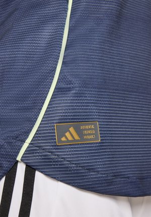 Tumes sinine sportlik särk tekstuuritud mustriga, mida kaunistavad helesinised äärised ja Adidas litsentsitud toote silt kuldse logo jaotisega.