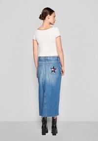 Hvit kortermet topp med rød kant, kombinert med et høyhals blått denimskjørt med en stjerneapplikasjon på baklommen. Svart ankelboots.