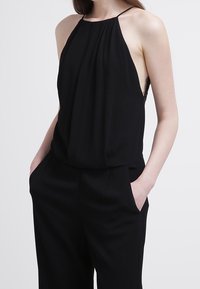 Haut noir à col licou avec plis, côtés ouverts et fines bretelles. Confectionné en tissu doux, il comprend des poches sur les côtés pour plus de fonctionnalité.