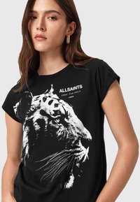 Camiseta de manga corta negra con un gráfico de tigre blanco, texto "ALLSAINTS", cuello redondo y mangas enrolladas. Material de algodón suave.