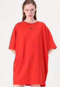 Rød oversized t-skjorte laget av myk bomull. Den har korte ermer, rund hals og en liten logo trykt på brystet.