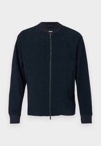 Námořnická bomber bunda se zipem vpředu, žebrovanými manžetami a límcem. Vyrobena z texturované tkaniny, obsahuje boční kapsy a má minimalistický design.