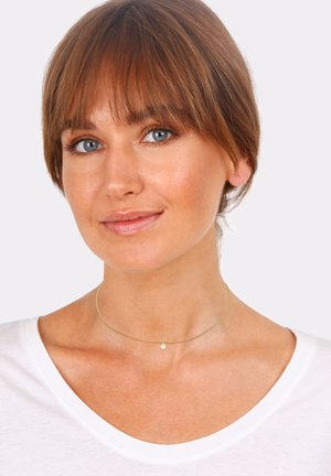 Goldene Choker-Halskette mit einer zarten Kette und einem kleinen, runden weißen Anhänger. Getragen mit einem weißen T-Shirt vor einem neutralen Hintergrund.
