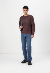 Rød og svart teksturert strikkegenser, avslappet passform, rund hals. Kombinert med blå rette bukser og svarte slip-on sko.
