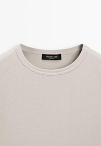 Licht beige katoenen t-shirt met een ronde halslijn, zachte textuur en geribbelde details bij de kraag. Label leest "Massimo Dutti."