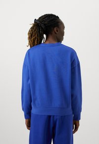 Μπλε φούτερ με άνετη γραμμή, ριμπ μανσέτες και στρίφωμα. Μαλακό ύφασμα, στρογγυλή λαιμόκοψη και διακριτική λεπτομέρεια στο πίσω μέρος. Συνδυάζεται με αντίστοιχα παντελόνια.