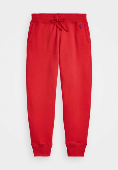 Red sweatpants made of soft fabric, featuring a drawstring waistband, two side pockets, and elastic cuffs. Small logo in blue on left thigh.