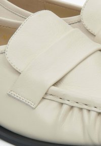 Cream leather flat shoe featuring a wide bow accent and gathered detailing along the front. Black sole with visible stitching.