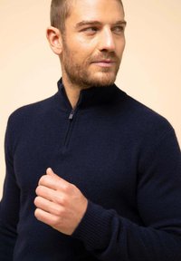 Granatowy sweter na zamek z wysokim kołnierzem, wykonany z teksturowanej tkaniny. Posiada wysoki kołnierz i ściągacze przy rękawach. Dopasowany krój.