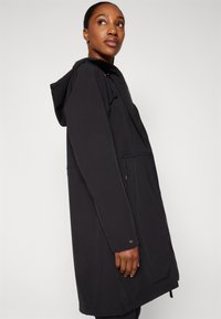Veste à capuche noire avec fermeture éclair, arborant une coupe décontractée, un tissu doux, des poches latérales et un cordon de serrage à la capuche.