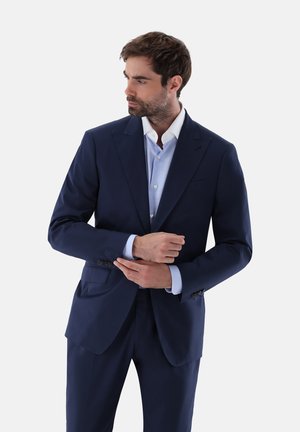 Giacca da abito blu navy con un design strutturato, dotata di rever a punte e chiusura con un solo bottone. Accompagnata da una camicia da uomo azzurro chiaro.