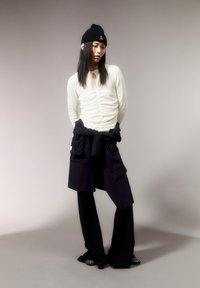 Witte gerimpelde lange mouw top, zwarte muts, marineblauw streeppatroon rond de taille, zwarte flared broek, versierde zwarte schoenen, gladde textuur.