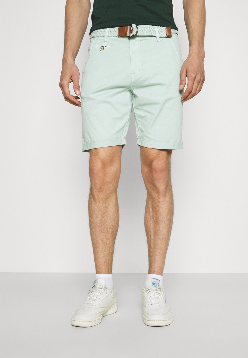 Shorts vert menthe en tissu léger, dotés d'une taille ceinturée, de détails de poche à bouton et d'ourlets retroussés. Portés avec des baskets blanches.