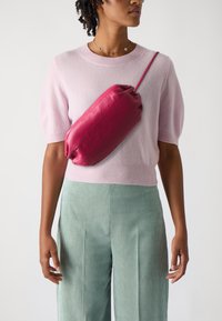 Fuchsia lærveske med myk, rund form, som har en enkelt stropp. Brukt over en lys rosa genser og stripete teal bukser.
