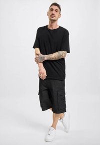Zwart T-shirt met korte mouwen, gecombineerd met donkergrijze cargoshorts met twee voorzakken, gedragen met witte sneakers. Glad materiaal en een ontspannen pasvorm.