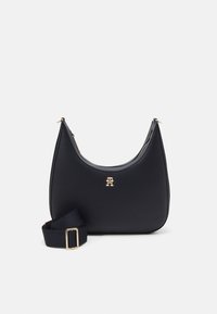 Schwarze Lederhandtasche mit geschwungener Form, goldfarbener Logo-Akzent und abnehmbarem schwarzen Tragegurt. Glatte Textur und Reißverschluss.