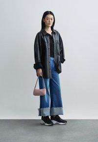 Black leather oversized shirt, black top, wide-leg denim jeans with frayed hems, black and white sneakers, and a small pink handbag.