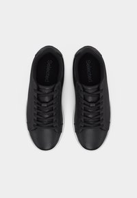 Ζευγάρι μαύρα αθλητικά παπούτσια με κορδόνια και λευκές σόλες, φωτογραφημένα από πάνω σε λευκό φόντο.