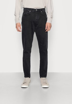 Jeans de mezclilla negra con un corte ajustado, con diseño de cinco bolsillos, costuras a tono y cierre de botones clásico. Llevados con zapatillas ligeras.