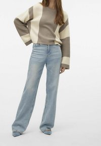 Pull en tricot à rayures horizontales beige et crème, manches larges. Assorti à un jean taille haute bleu clair et des chaussures à bouts pointus.