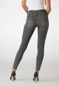 Sittande grå denimjeans med en klassisk femfickdesign och subtila blekningar, kombinerat med svarta högklackade skor.