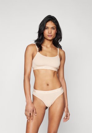 Nude bralette and matching thong set made of soft fabric, featuring thin straps and a branded elastic waistband. Smooth texture, minimalist design.