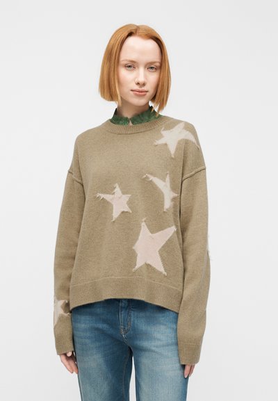 Πουλόβερ σε χακί χρώμα με πλεκτό σχέδιο ροζ αστεριών, στρογγυλή λαιμόκοψη και ραφές στους ώμους που κατεβαίνουν, συνδυασμένο με πράσινο πουκάμισο με γιακά από κάτω.