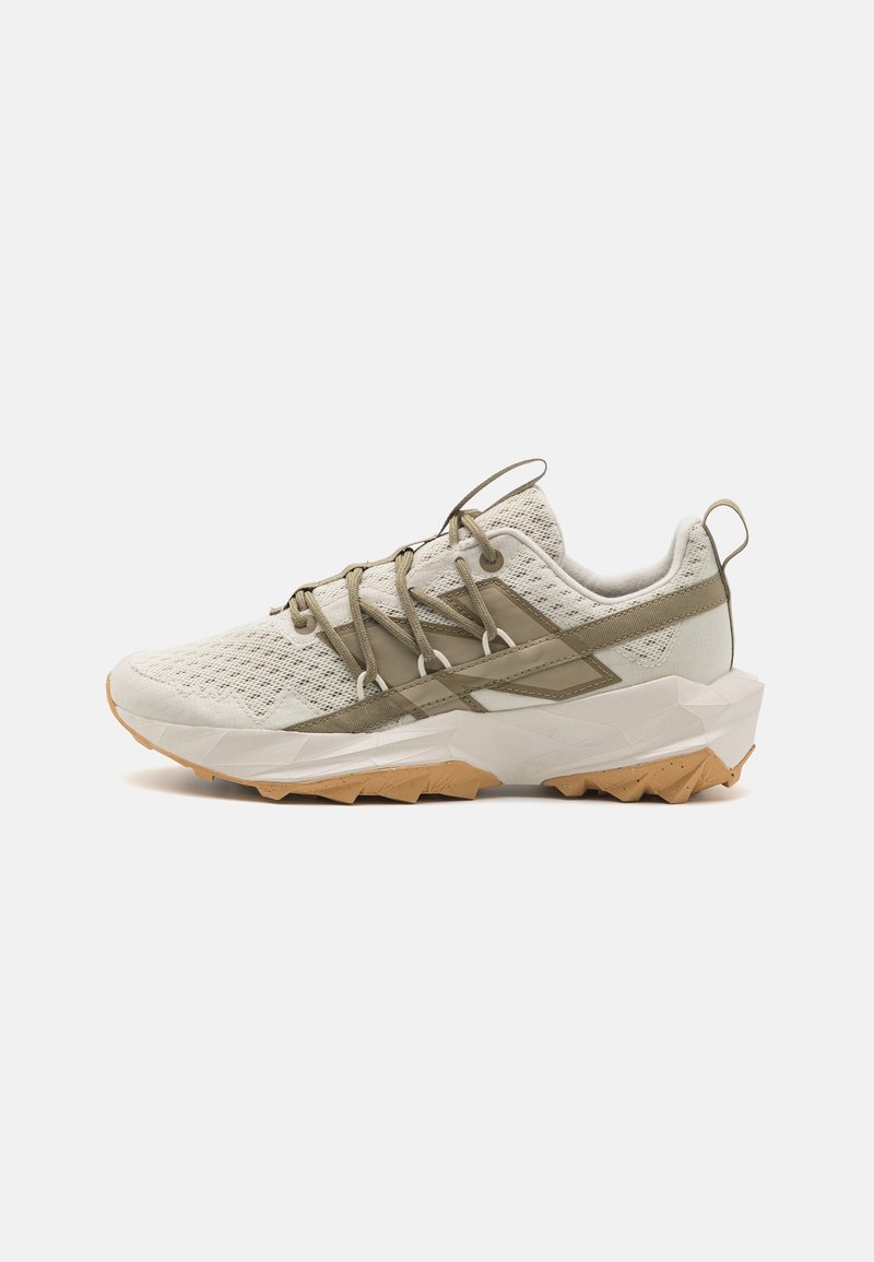 Basket de sport beige clair avec dessus en mesh, touches de vert olive, semelle blanche épaisse, semelle extérieure beige robuste et languettes au talon et sur la languette.