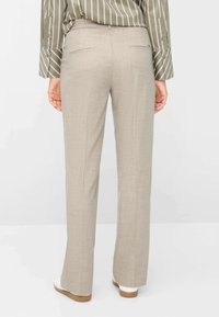 Beige op maat gemaakte broek met rechte pijpen, achterzakken en een gladde textuur; gecombineerd met een groen-wit gestreept shirt.